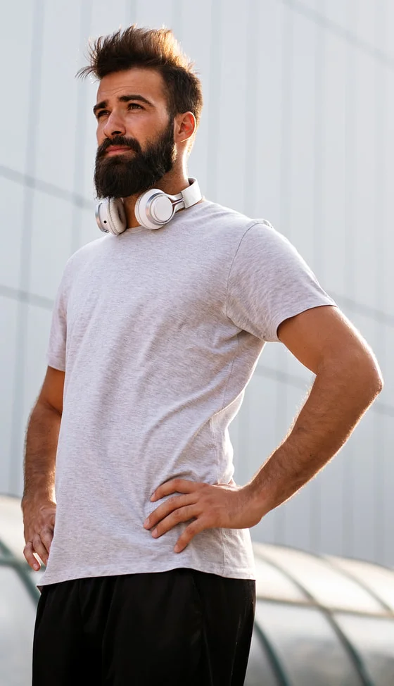A bearded man outdoors after a workout, headphones around his neck